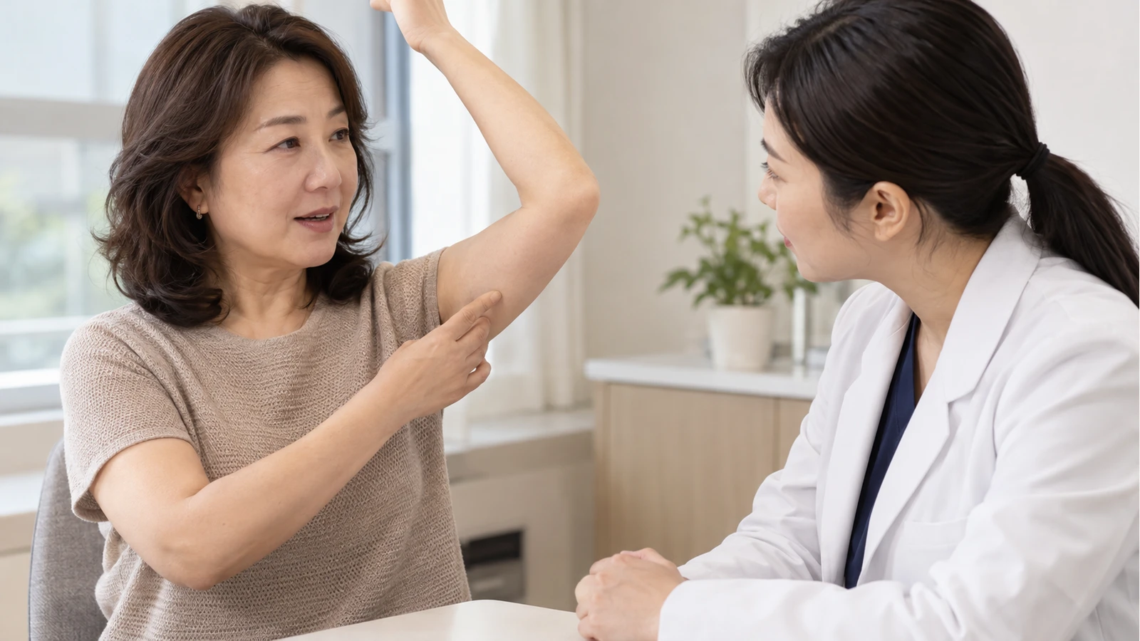 여성이 들어 올린 팔 안쪽을 손가락으로 가리키며 의료진 역할의 여성에게 설명하는 모습